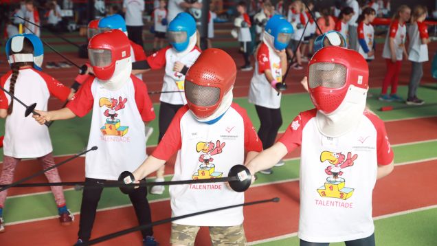 Foto von Drittklässlern in Reihe mit Talentiade-Shirts und Fechtmasken beim Probe-Fechten