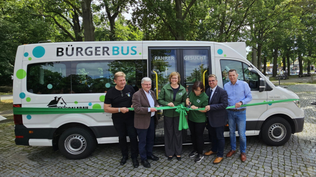 Foto des Bürgerbusses mit beteiligten Personen davor, die symbolisch ein Band durchschneiden