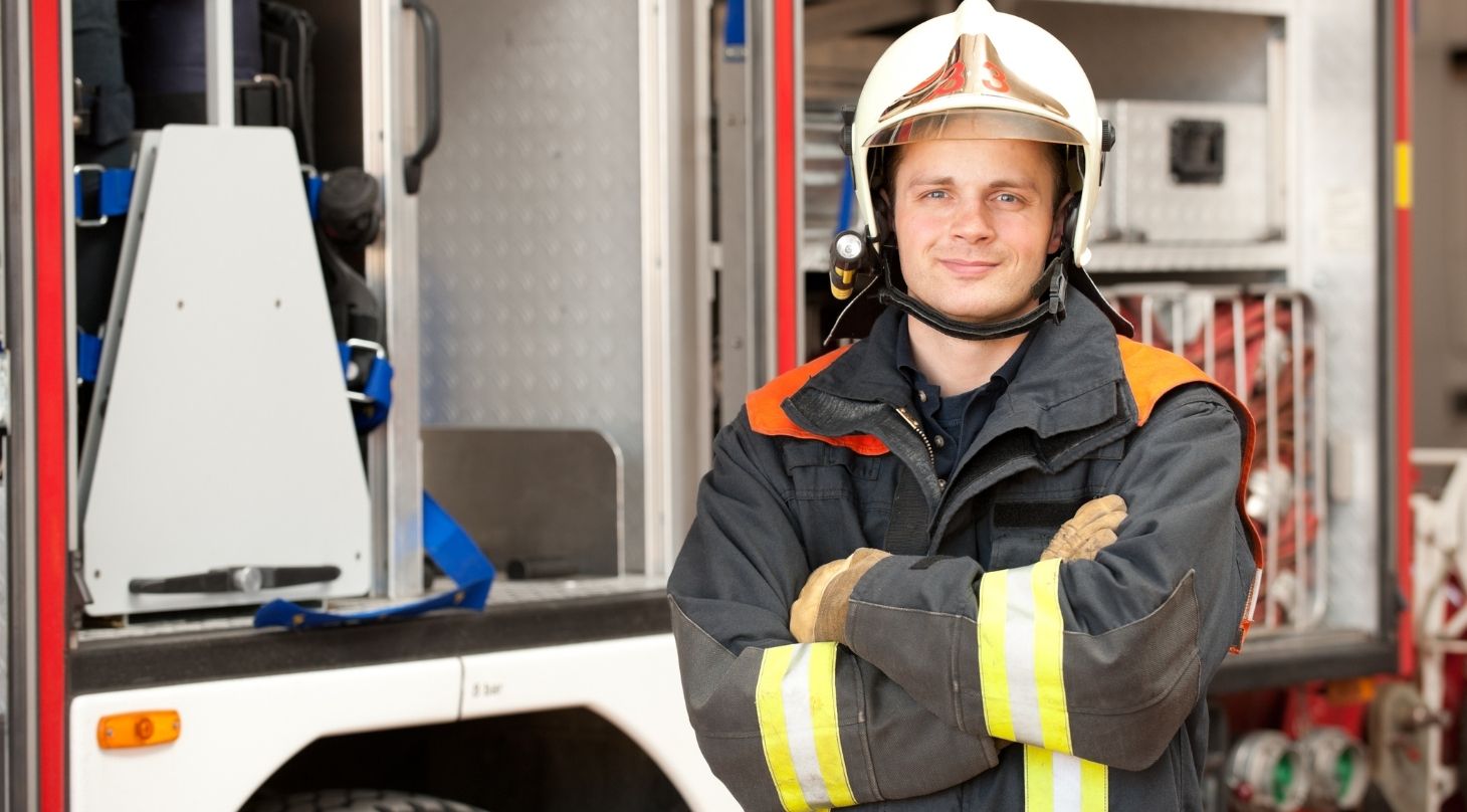 Foto von jungem Feuerwehrmann mit verschränkten Armen vor einem Fahrzeug