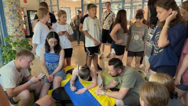 Foto einer Gruppe von Kindern und Jugendlichen beim Beschriften einer ukrainischen Fahne