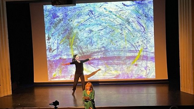 Foto der Performance Glücksmomente auf einer Bühne mit zwei Personen und großem malerischen Leinwandbild im Hintergrund