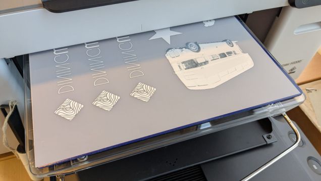 Foto des Textildrucksystems Direct-To-Film in Form eines grauen Druckers mit aufliegender Druckplatte
