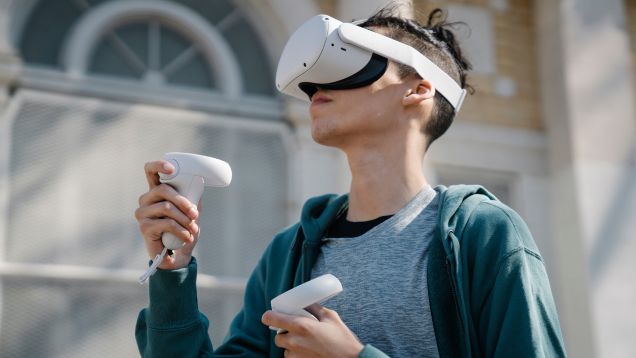 Foto eines Jungen im grünen Hoodie mit aufgesetzter VR-Brille und Controllern in den erhobenen Händen