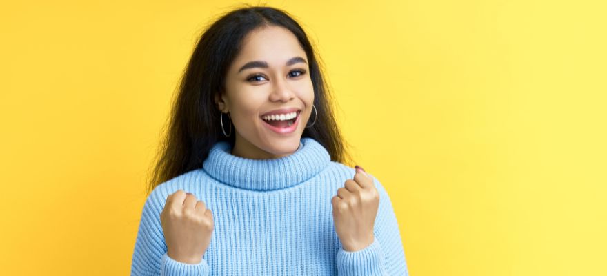 77.777 Euro im Spiel 77 gewonnen Frau mit blauem Pulli freut sich vor gelben Hintergrund